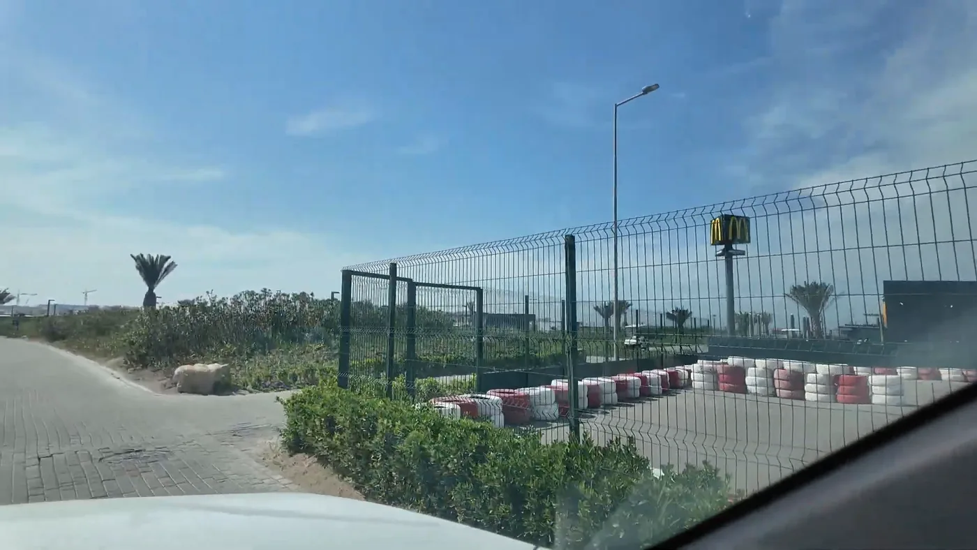 The neighbor on the street is a McDonald's; its sign shows above the track fence (May 2025)